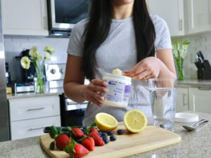 Woman scooping prime Fertility powder into a drink with fresh fruits 