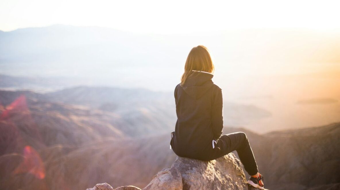 Woman sitting on mountain top, watching the sunset with her back to the camera