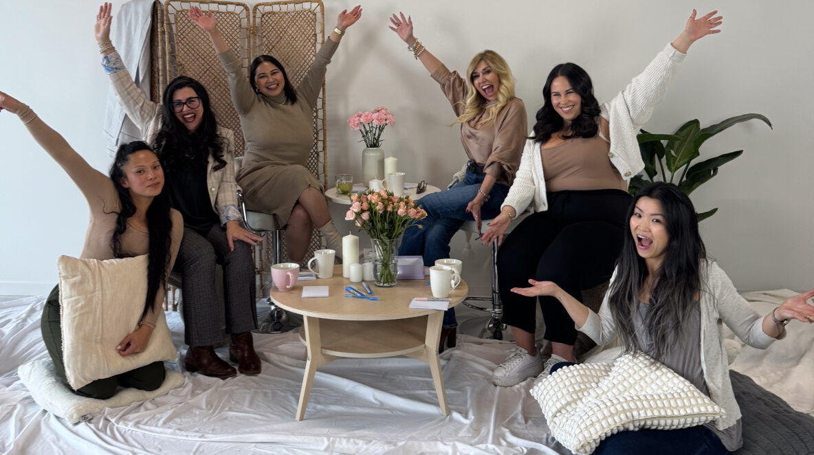 Six women gathered for a group discussion smiling and waving