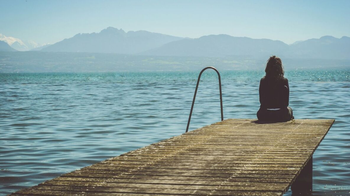 Woman sitting at the end of a jetty facing the water