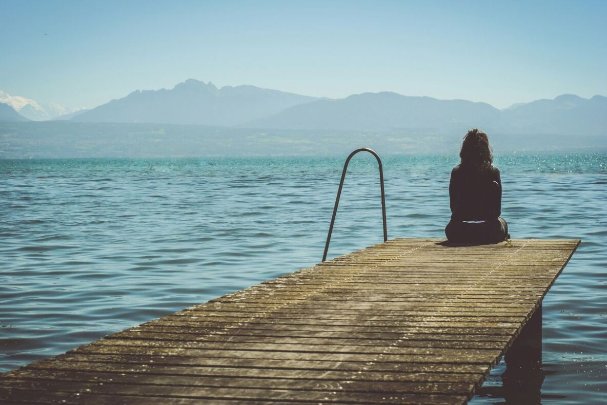 Woman sitting at the end of a jetty facing the water