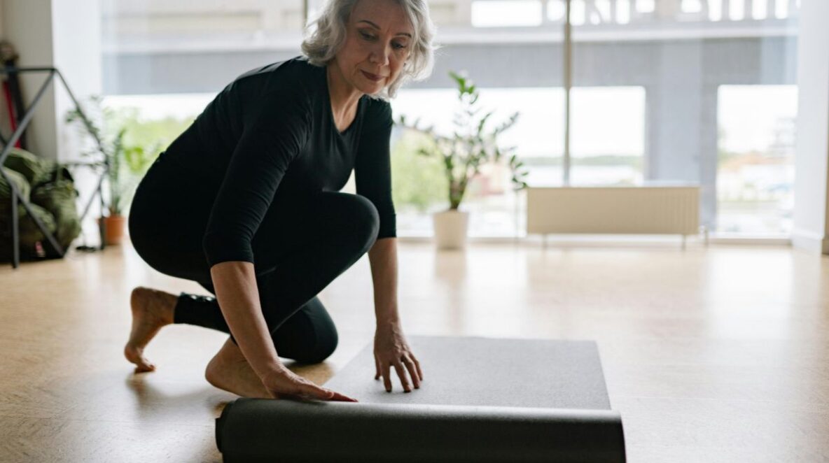 Mature woman rolling out yoga mat on the floor