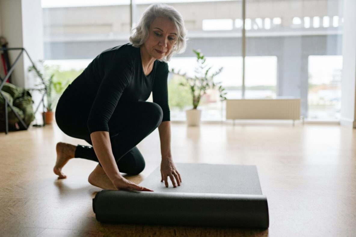 Mature woman rolling out yoga mat on the floor